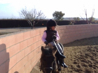 nina montando en un recinto cerrado montando a caballo